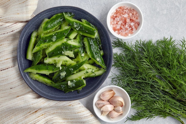 Zertrümmerte leicht gesalzene zerbrochene Gurken in einer Keramikschale mit rosafarbenem Salz-Knoblauch-Dill und Küchentuch-Serviette