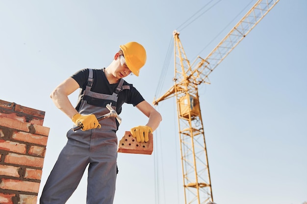 Ziegel halten und Hammer verwenden Bauarbeiter in Uniform und Sicherheitsausrüstung haben Arbeit am Bau