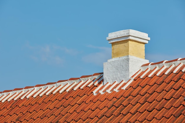 Ziegelschornstein auf Schieferdach des Hausgebäudes draußen vor blauem Himmelshintergrund Bau der Außenarchitektur der Fluchtrutsche, die auf dem Dach für Rauch und Hitze des Kamins gebaut wurde