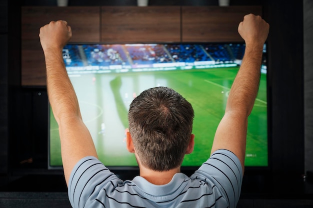 Ziel emotionaler Fan, der bei Nacht Fußball von hinten sieht Mann, der zu Hause ein Fußballspiel im Fernsehen ansieht