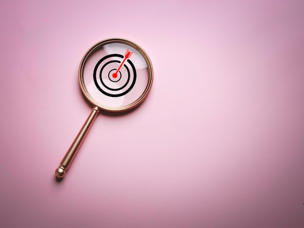 Zieltafel innerhalb des Lupenglases für Fokusgeschäftsziel-Zielsuchkonzept und Erfolg auf rosa Hintergrund und Kopienraum