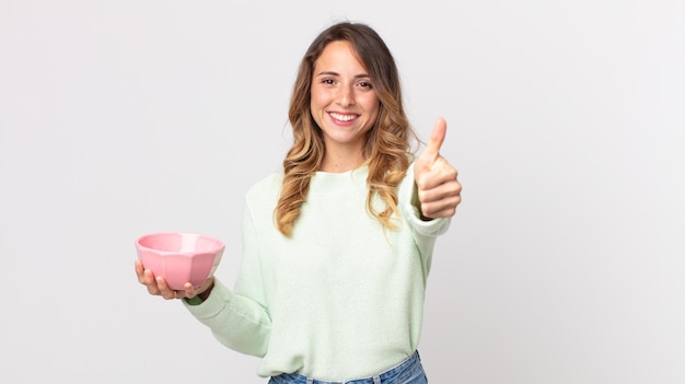 Ziemlich dünne Frau, die sich stolz fühlt, positiv mit erhobenen Daumen lächelt und eine leere Topfschale hält