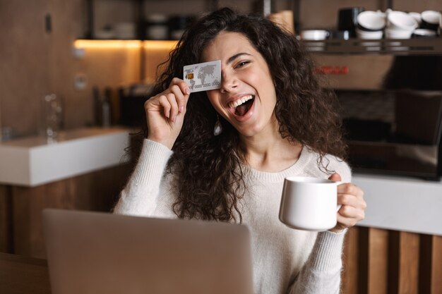 ziemlich emotionales Mädchen sitzt im Café mit Laptop-Computer mit Kreditkarte