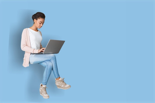 Ziemlich fröhliche Frau, die auf pastellfarbenem blauem Hintergrund auf dem Laptop tippt