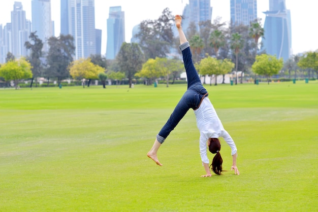 ziemlich gesunde junge Frau springt und trainiert Fitness auf Gras im grünen Park mit Stadt im Hintergrund