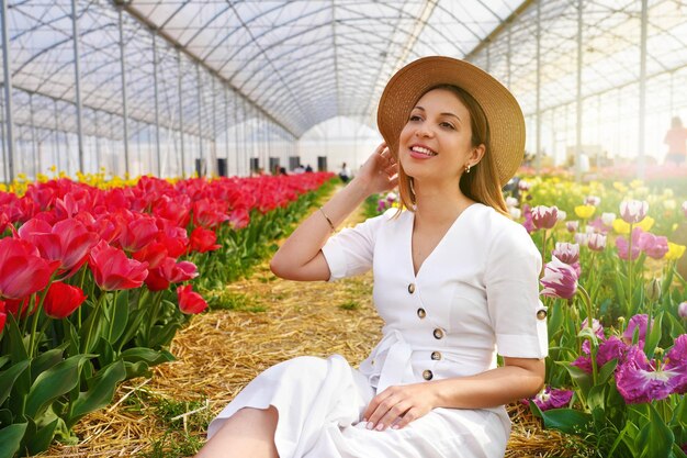 Ziemlich schönes Mädchen mit Strohhut, das zwischen Tulpenfeldern im Gewächshaus sitzt