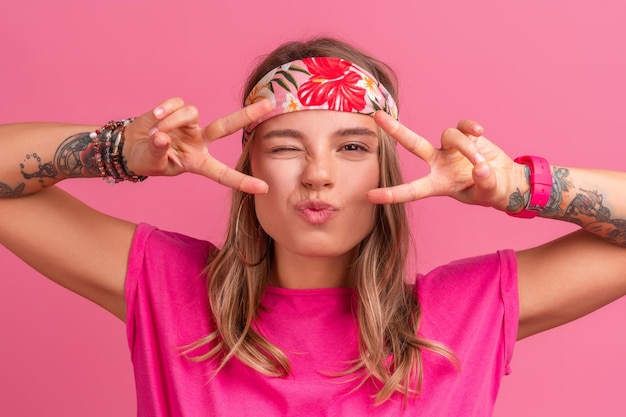 Ziemlich süße lächelnde Frau in rosafarbenem Hemd im Boho-Hippie-Stil mit Accessoires, die emotionalen Spaß lächelt und auf rosafarbenem Hintergrund posiert, isoliert positive Stimmung