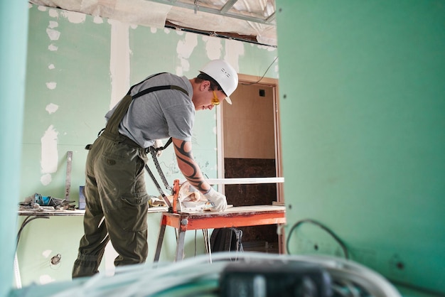 Zimmer reparieren. Baumeister schneidet Fliesen auf einer Baustelle