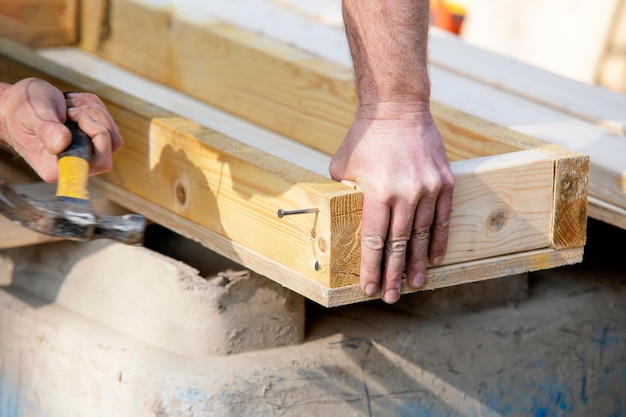 Zimmermann hämmert Nagel mit Hammer in das Holz Tischler mit Hammer und Nagel Nahaufnahme