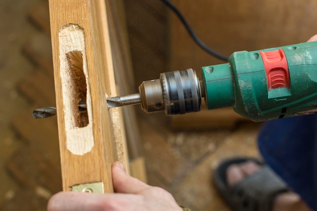 Zimmermann macht ein Loch in der alten Holztür das Einsteckschloss für die Verwendung einer Bohrmaschine. Nahansicht.