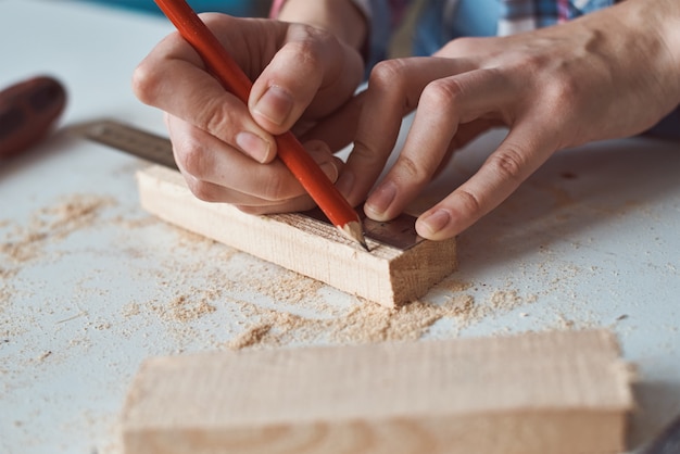 Zimmermannshände, die Messung mit Bleistift der Holzplanke nehmen. Konzept der DIY Holzarbeiten und Möbelherstellung