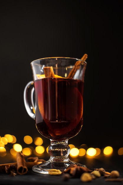 Zimt liegt in einem Glas, in einem Nahaufnahmeglas Glühwein mit Orange und in einem Zimt auf dunklem schwarzem Hintergrund