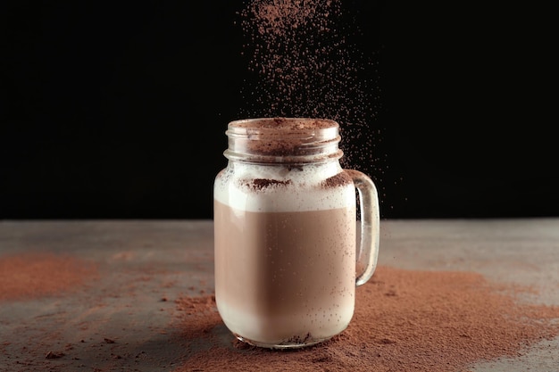 Zimtpulver in Einmachglas mit Latte Macchiato auf schwarzem Hintergrund gießen