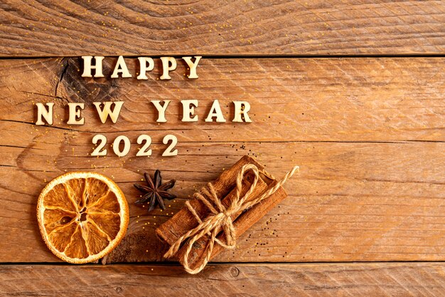 Zimtstangen, getrocknete Orangenscheiben, Sternanis und Zitat Frohes neues Jahr 2022 auf Holzhintergrund