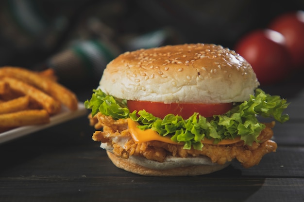 Zinger Burger auf dunklem Holztisch mit Pommes und Tomaten im Hintergrund