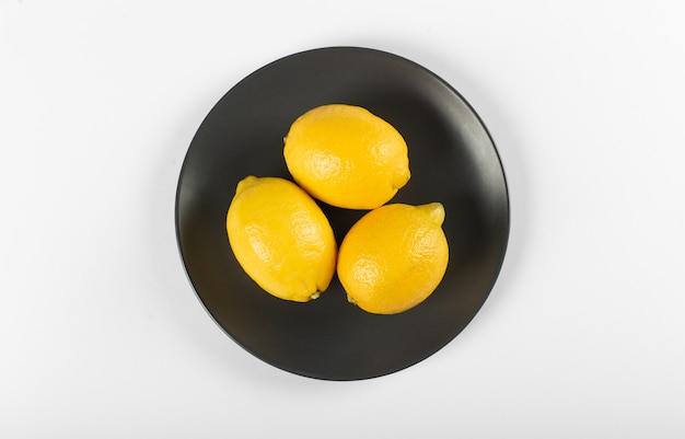 Zitronen auf einer schwarzen Untertasse lokalisiert auf Weiß. Draufsicht