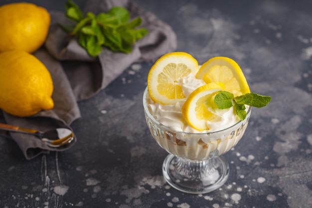 Zitronendessert. Englische Zitronen, Käsekuchen, Schlagsahne, Parfait. Fruchtkremeis im Glas auf einem dunklen Hintergrund.