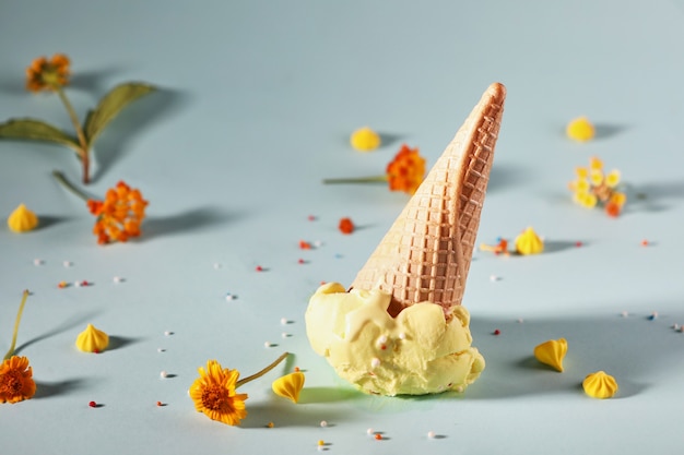 Zitroneneis mit Waffelkegel auf blauem Hintergrund mit gelben Blüten.