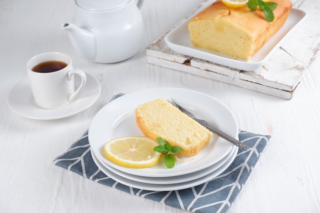 Zitronenkuchen mit weißer Teekanne und einer Tasse Kaffee mit verschwommenem Hintergrundweißer Hintergrund