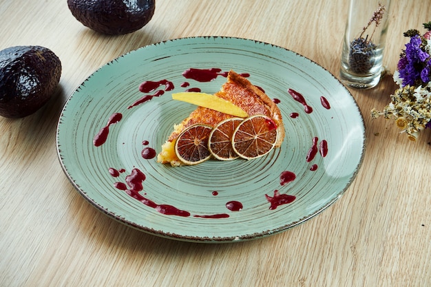 Zitronenkuchenscheibe mit roter süßer Soße auf einem blauen Teller auf einem Holztisch. Leckeres Gebäck für Tee oder Kaffee. Nahansicht. Leckeres Essen