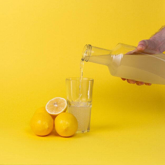 Zitronensaft wird in ein Glas mit einer Glasflasche gegossen Ganze und geschnittene Zitronen liegen in der Nähe