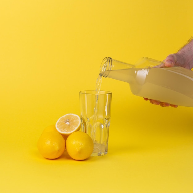 Zitronensaft wird in ein Glas mit einer Glasflasche gegossen Ganze und geschnittene Zitronen liegen in der Nähe