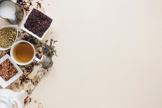 Foto zitronentee mit trockenen teeblättern; getrocknete chinesische chrysanthemenblüten; teesieb; milch; kräuter und teekanne auf farbigem hintergrund