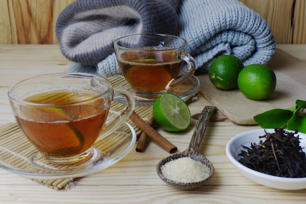Foto zitronenteegläser mit winterkleidung und grüner zitrone mit zucker und teeblättern auf holztisch.