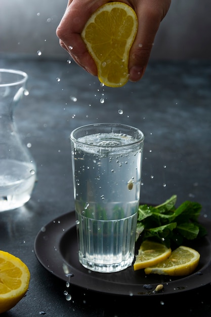 Zitronenwasser, Getränk zur Stärkung des Immunsystems. Hand, die frischen Zitronensaft in einem Glas Mineralwasser auspresst. Sommergetränk.