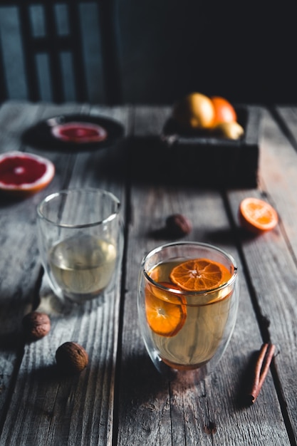 Zitrus-Tee in einer transparenten Teekanne und einem Glas, gesundes Getränk auf einem hölzernen Hintergrund.