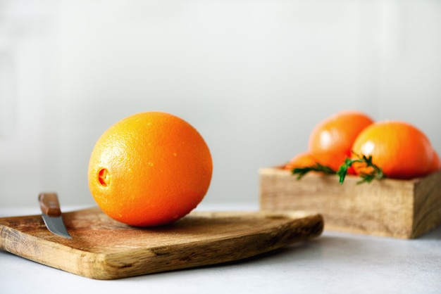 Zitrusfrüchte. Frisches Obst, Rosmarin. Große orange Frucht mit Wassertropfen, Messer, hölzernes Schneidebrett