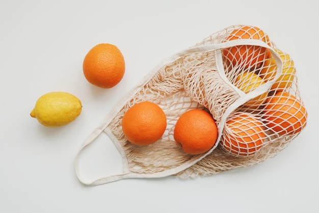 Zitrusfrüchte in wiederverwendbarer Tasche auf weißem Hintergrund flach liegen Draufsicht Kopierraum