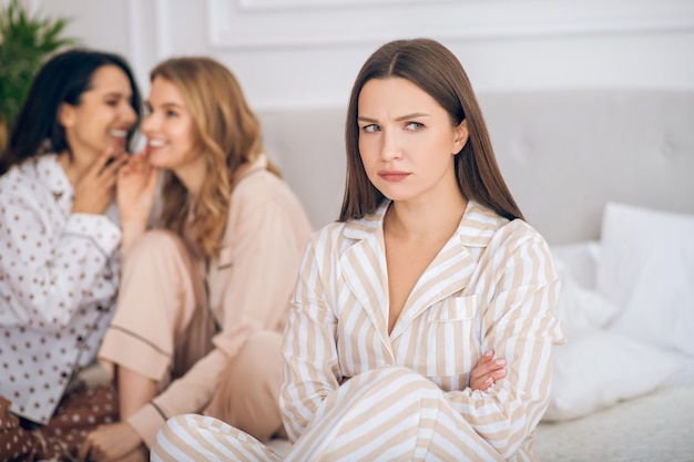 Zombaria. Duas meninas sentadas em uma cama conversando sobre a amiga pelas costas