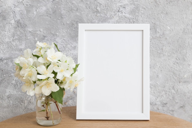 Zombe de moldura branca vazia em uma mesa redonda com flores de jasmim em um fundo cinza. Coloque seu texto ou imagem