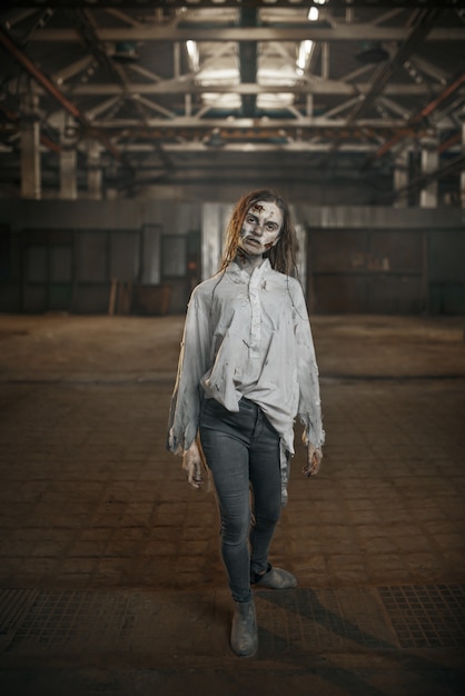 Zombie femenino caminando en fábrica abandonada, horror