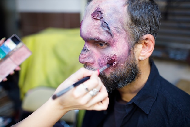 Zombie männliches Make-up, das sich für Halloween-Konzept bewirbt. Make-up mit Pinsel und Farbe Haut und Blutgesicht