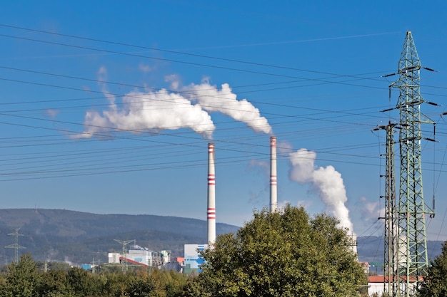 Zona industrial com tubos e exaustão contra o céu e vegetação