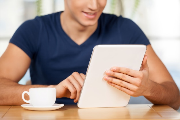 Zona wifi gratuita. Imagen recortada de un joven alegre con tableta digital mientras está sentado en el restaurante