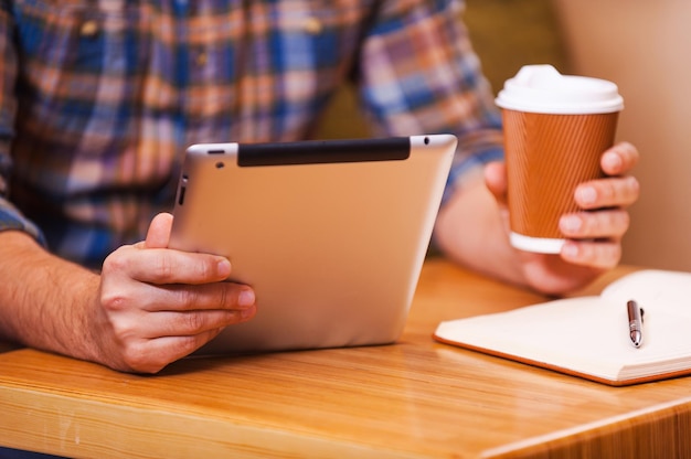 Zona wifi gratuita. Primer plano del hombre que sostiene la tableta digital y una taza de café mientras está sentado en el escritorio de madera