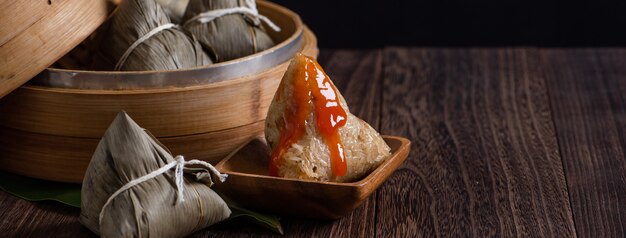 Zongzi. Bola de masa de arroz para el Festival del Barco del Dragón tradicional chino (Festival Duanwu) sobre fondo de mesa de madera oscura.