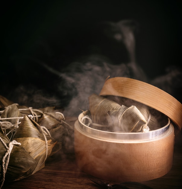 Foto zongzi, bolas de masa de arroz al vapor en vaporera sobre mesa de madera, famosa comida sabrosa en el concepto de diseño del festival del barco del dragón duanwu, de cerca, espacio de copia.