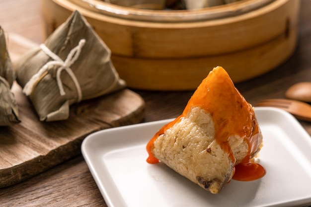 Zongzi Dragon Boat Festival Reisknödel essen junge asiatische Frau, die chinesisches traditionelles Essen auf Holztisch zu Hause isst, Feier aus nächster Nähe