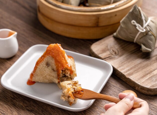 Zongzi Dragon Boat Festival Reisknödel essen junge asiatische Frau, die chinesisches traditionelles Essen auf Holztisch zu Hause isst, Feier aus nächster Nähe