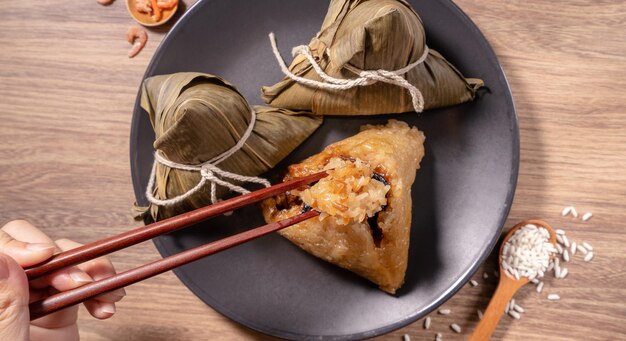 Zongzi-frau, die gedünstete reisknödel auf holztischessen im drachenbootfestival duanwu-konzept isst, nahaufnahme, kopierraum, draufsicht, flach liegend