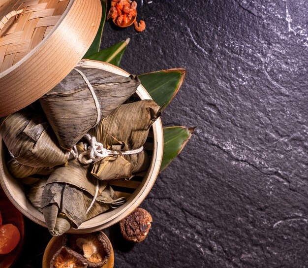 Zongzi köstliche gedämpfte Reisknödel im Dampfgarer auf schwarzem Hintergrund für das Drachenboot-Duanwu-Festival, Nahaufnahme, Kopienraum, Draufsicht, flach gelegt