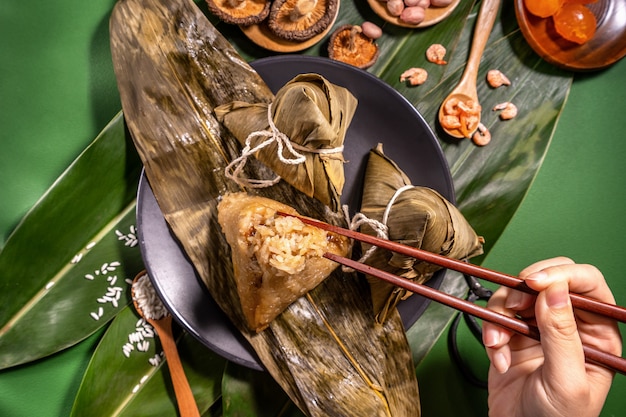 Zongzi, mujer comiendo albóndigas de arroz al vapor sobre fondo de mesa verde, comida en el concepto duanwu del festival del barco del dragón, de cerca, espacio de copia, vista superior, endecha plana