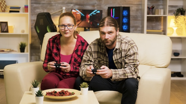 Zoom en la toma de la hermosa joven pareja jugando videojuegos sentados en el sofá con controladores.