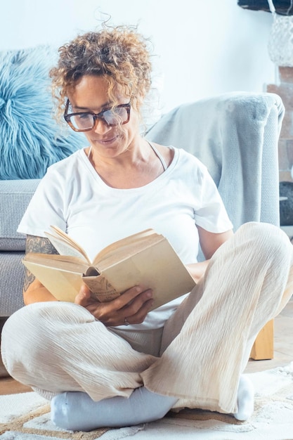 Foto zu hause bleiben, zeitvertreib, boomer, reife frau sitzt mit einem offenen buch drinnen auf dem boden, schöne junge dame liest eine aufregende geschichte, genießt einen faulen morgen, hat ein entspannendes wochenende, freizeitaktivität.