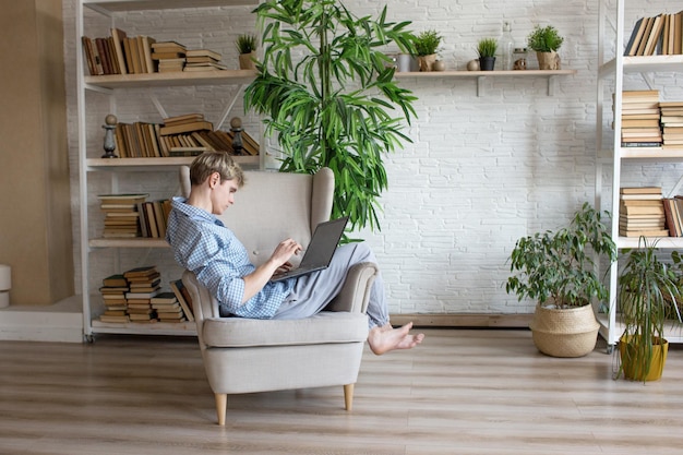 Zu Hause im Internet surfen Ein gutaussehender junger Mann arbeitet an einem Laptop, der in einem großen bequemen Sitz sitzt