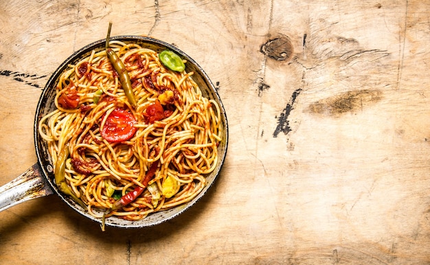 Zubereitete Spaghetti in Tomatensauce mit Gewürzen in der Pfanne. Auf hölzernem Hintergrund. Freier Platz für Text. Draufsicht